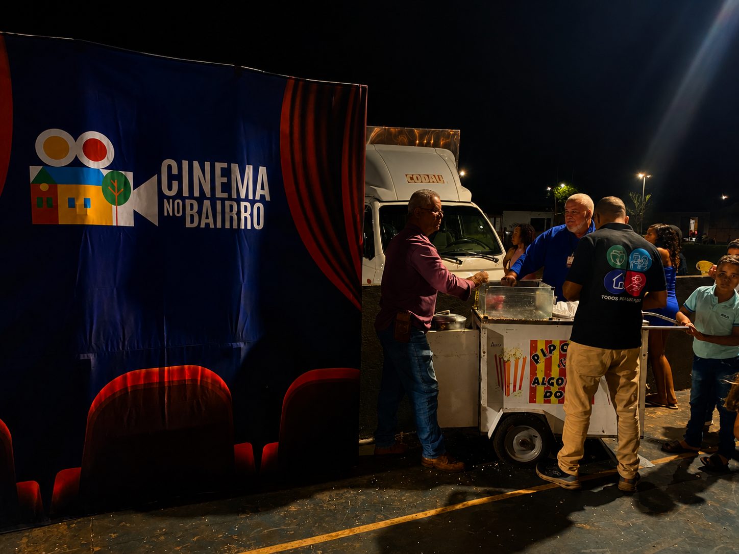 Carrinho de pipoca e algodão-doce ao lado do painel Cinema no Bairro