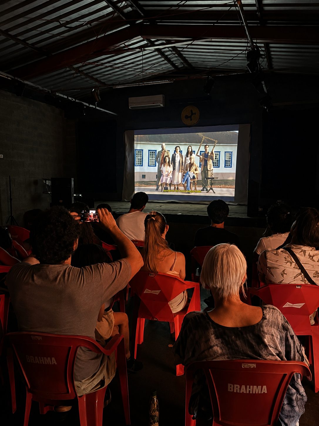 Plateia em cadeiras vermelhas diante da tela
